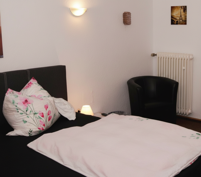 Ein einfaches Schlafzimmer mit einem Bett, einem Stuhl und gedämpfter Beleuchtung.