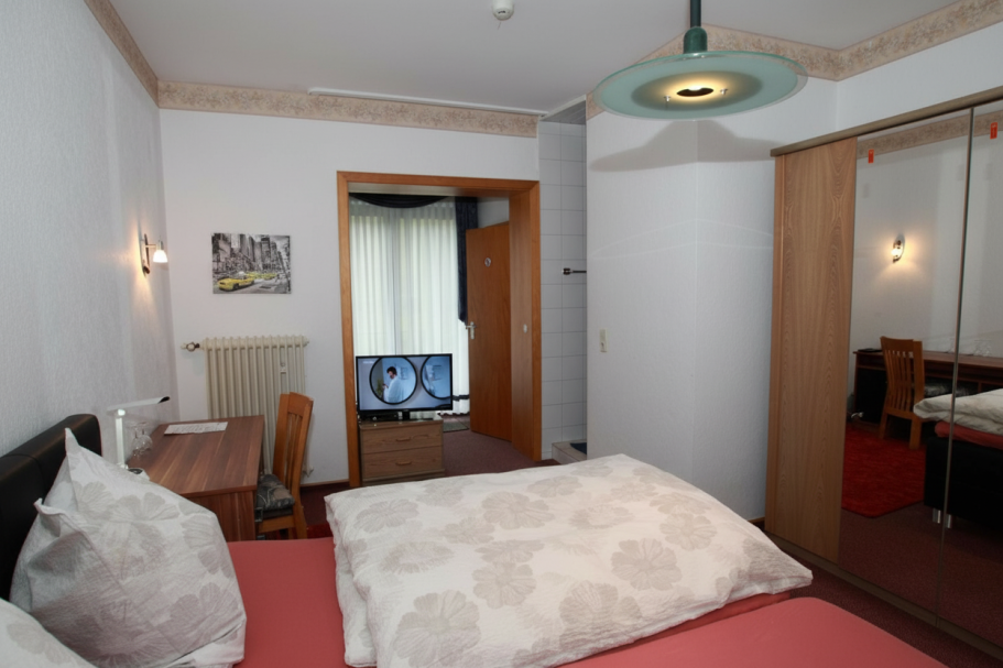 Gemütliches Schlafzimmer mit Doppelbett, Schreibtisch und einem Spiegel im Hintergrund.